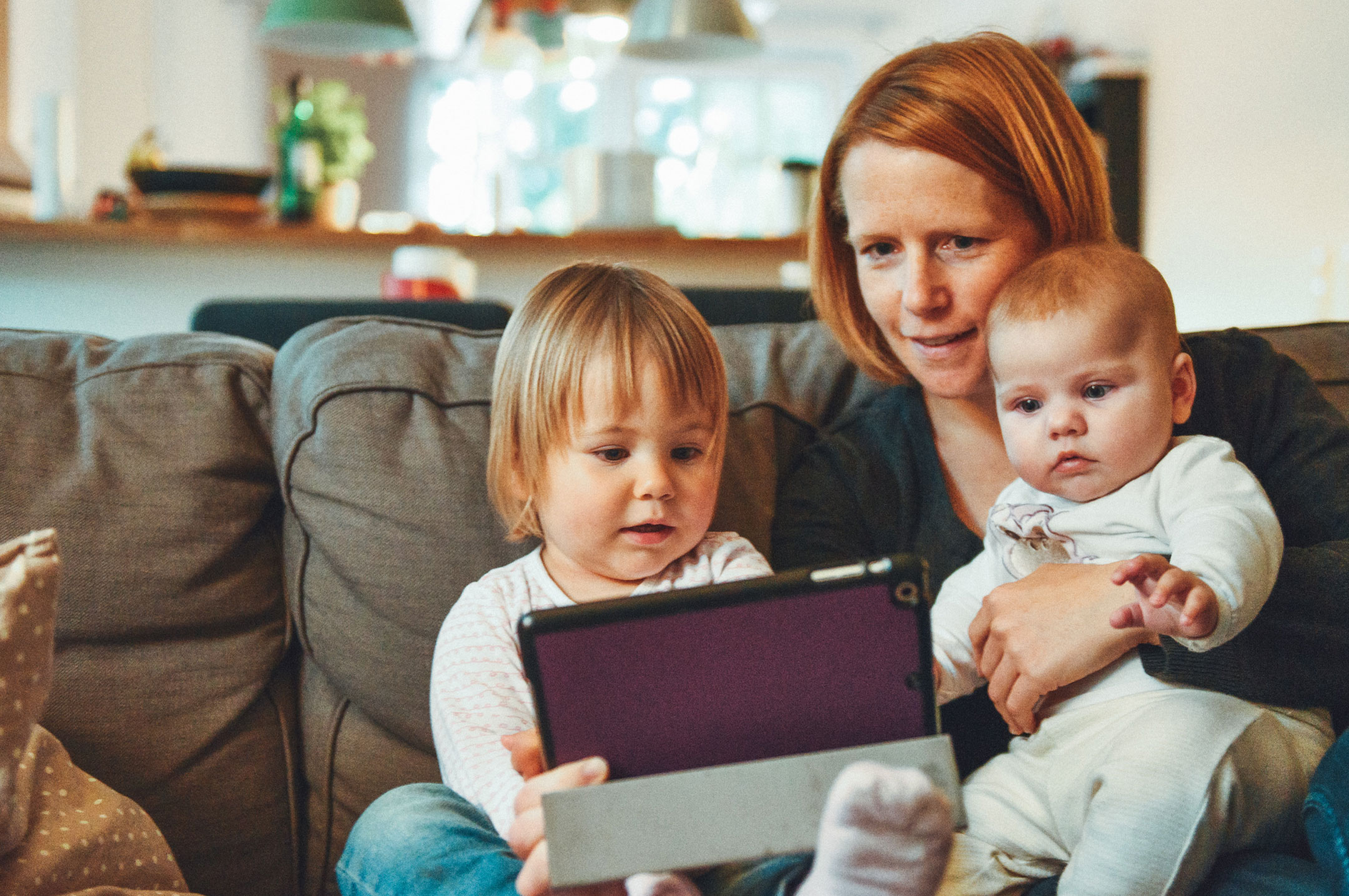 Woman holding two babies while looking at a tablet